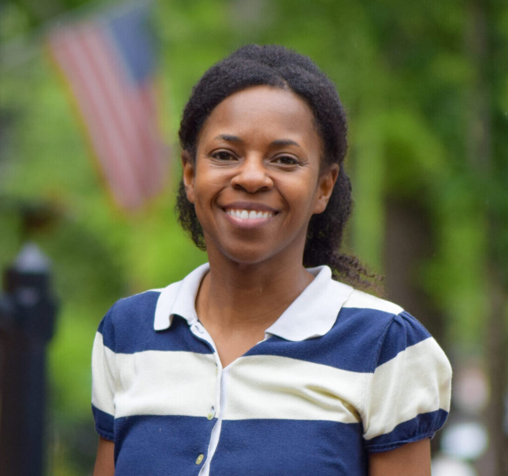 Smiling woman outdoors with an American flag in the background.