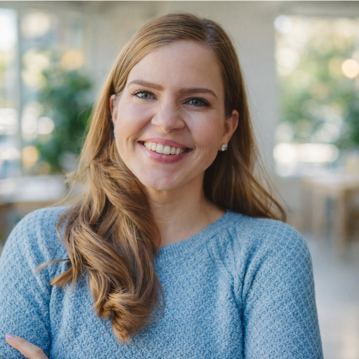 Smiling woman with long red hair wearing a light blue sweater in a bright office