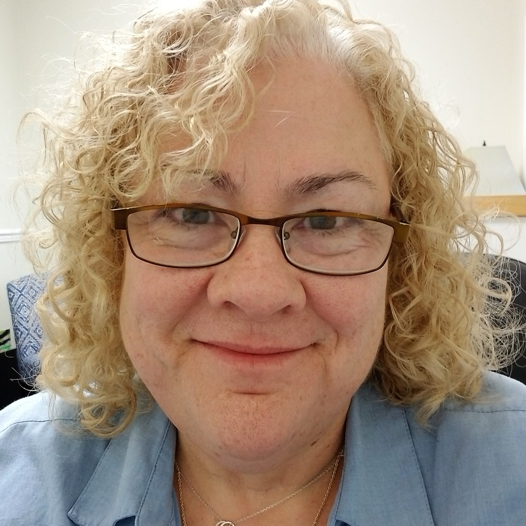 Christine Flood wearing glasses and a blue shirt, smiling warmly.