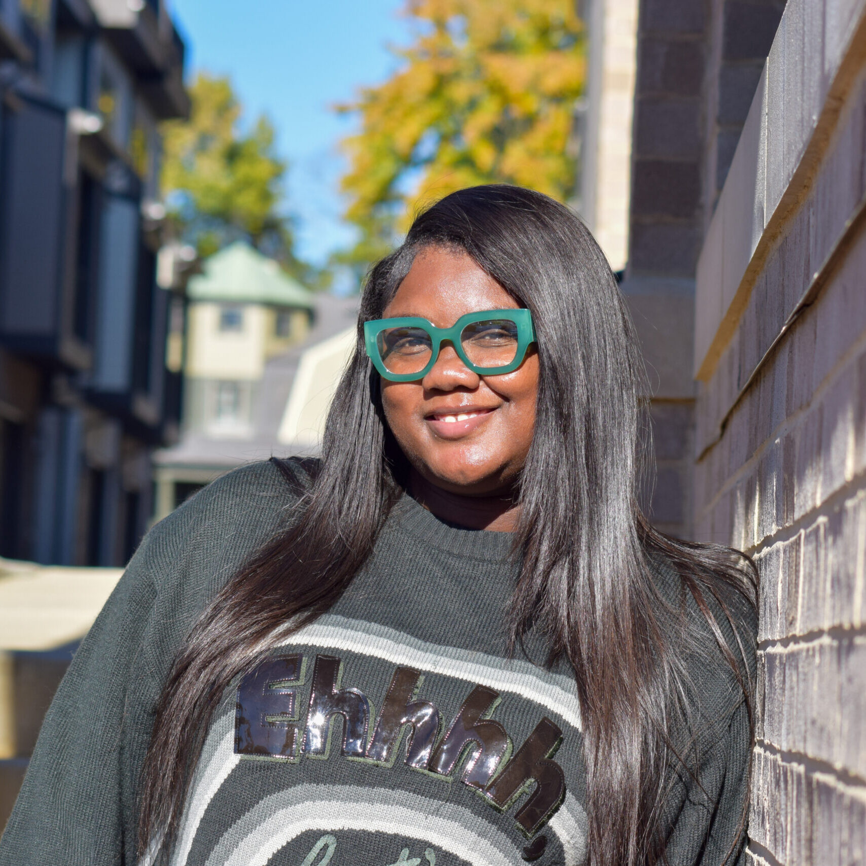 Smiling woman with long straight hair wearing green glasses and a black sweater outdoors.